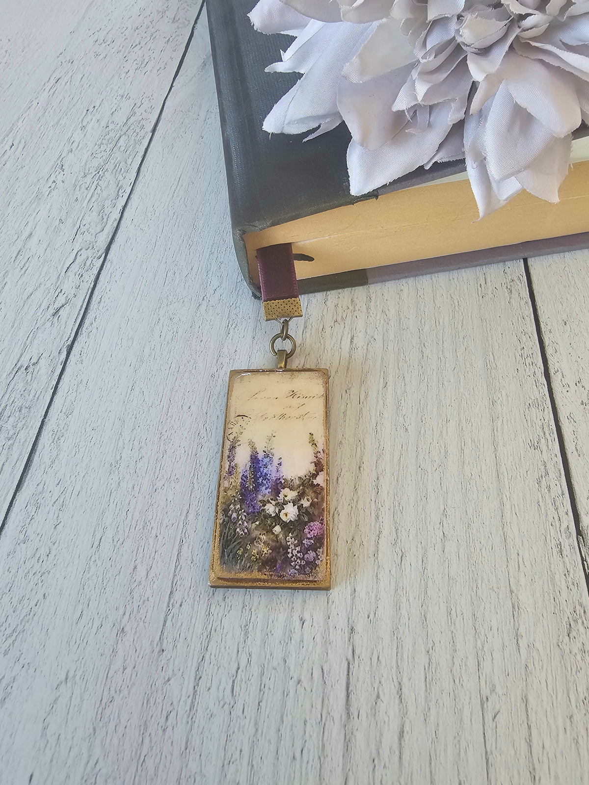 A rectangular pendant with a floral design is attached to a book's spine, resting on a white wooden surface.