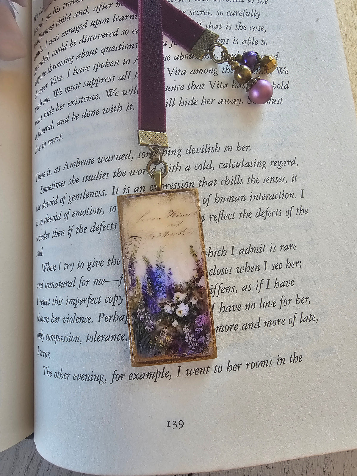 a book with a purple bookmark featuring a floral design, resting on an open page with text.