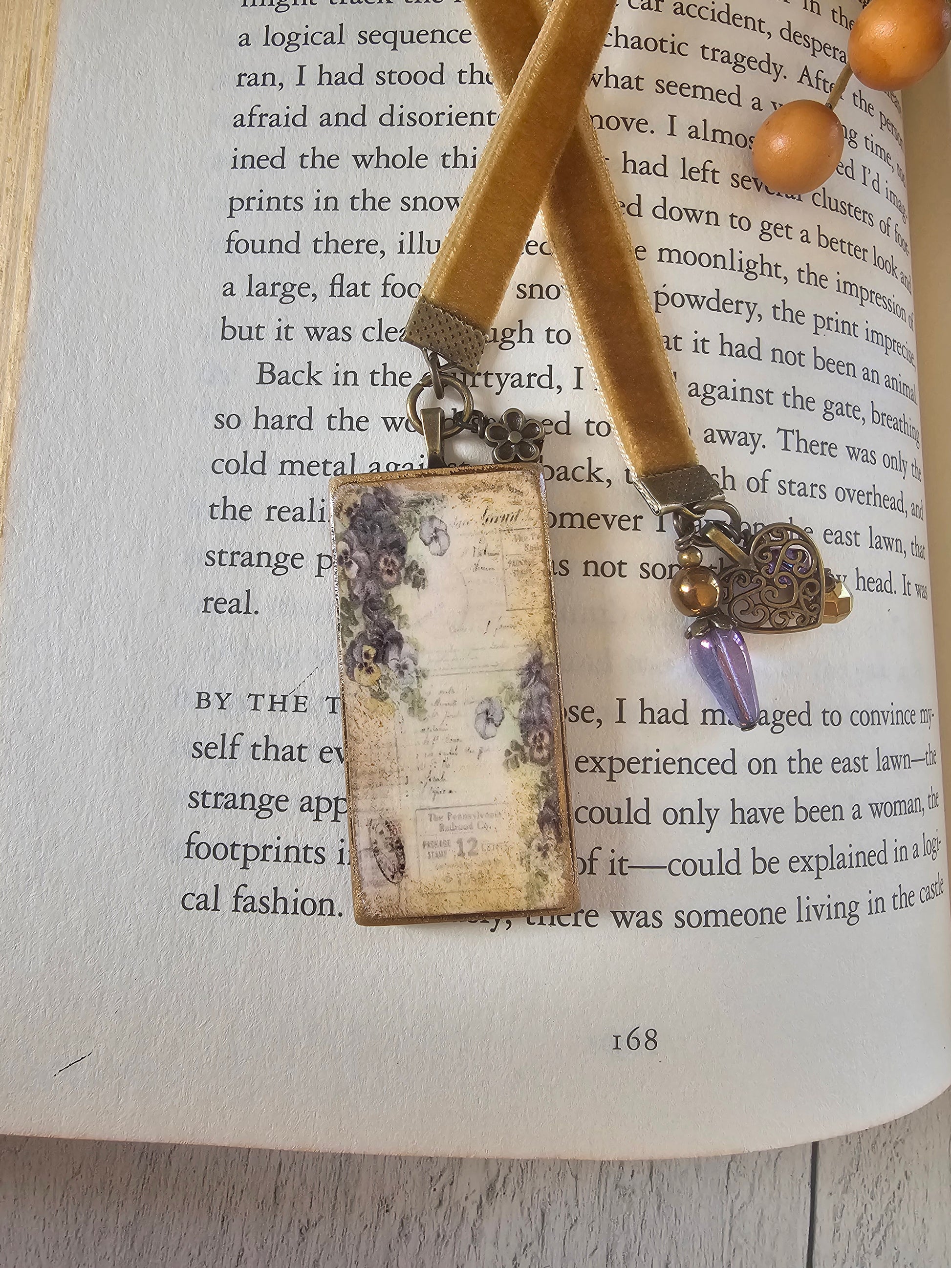 A vintage-style bookmark with a floral design rests on top of an open book, accompanied by a beaded necklace.