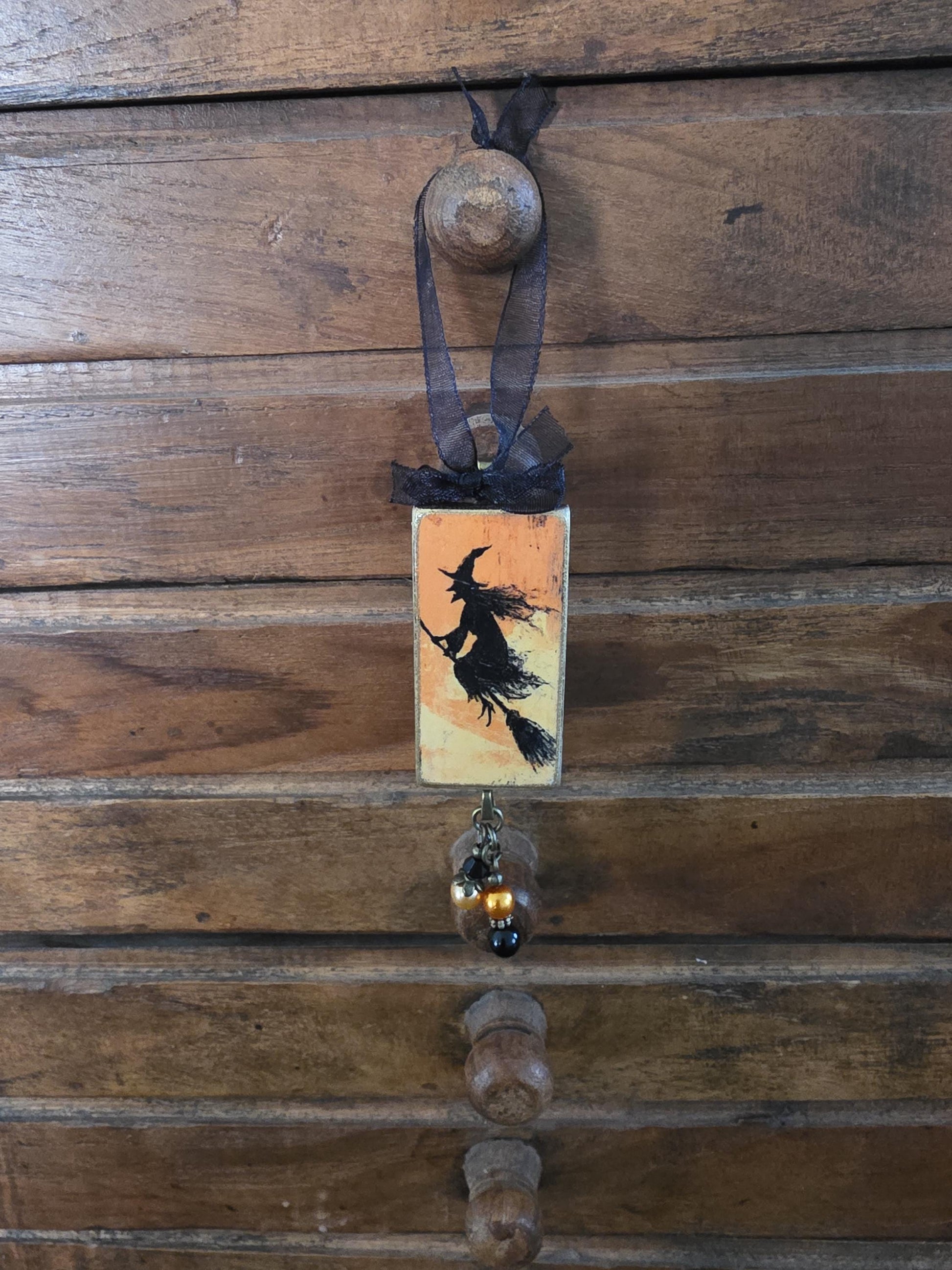 A wooden wall with a decorative piece featuring a silhouette of a witch on a broomstick, hanging from a hook.