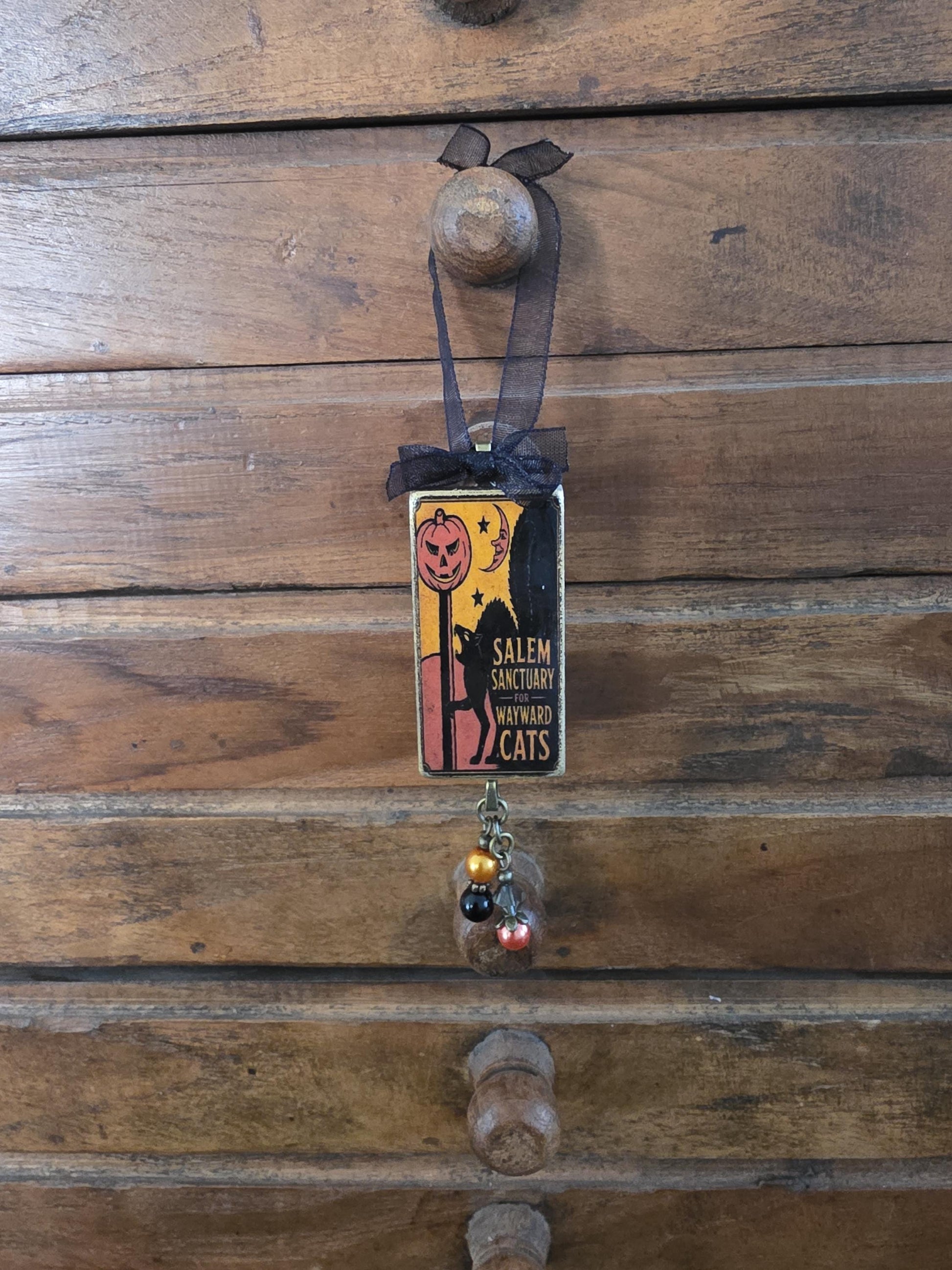 A Halloween-themed pendant hanging from a wooden drawer, featuring a pumpkin and a cat silhouette.