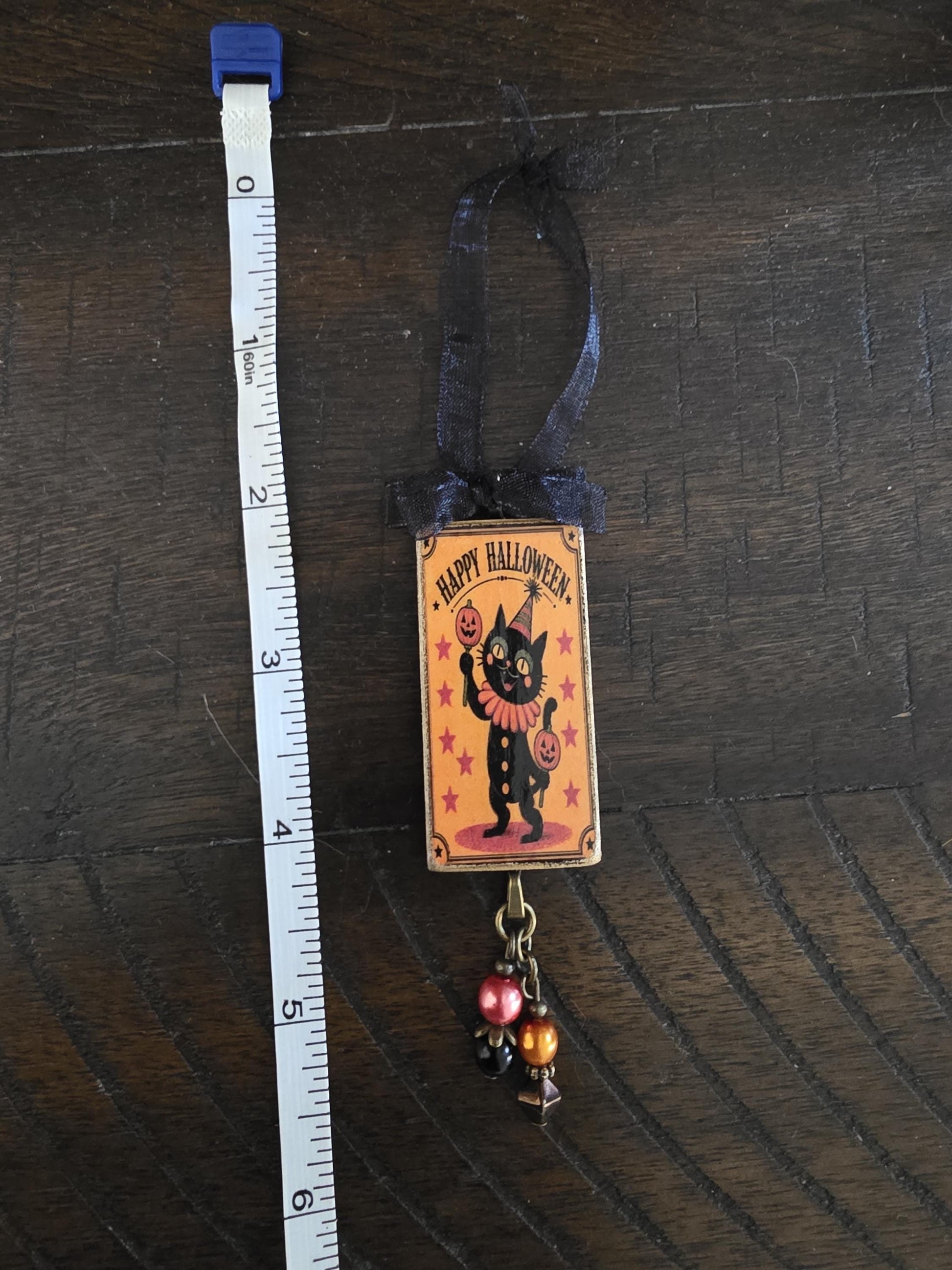 A Halloween-themed ornament with a cat and a "Happy Halloween" sign, hanging on a wooden surface.