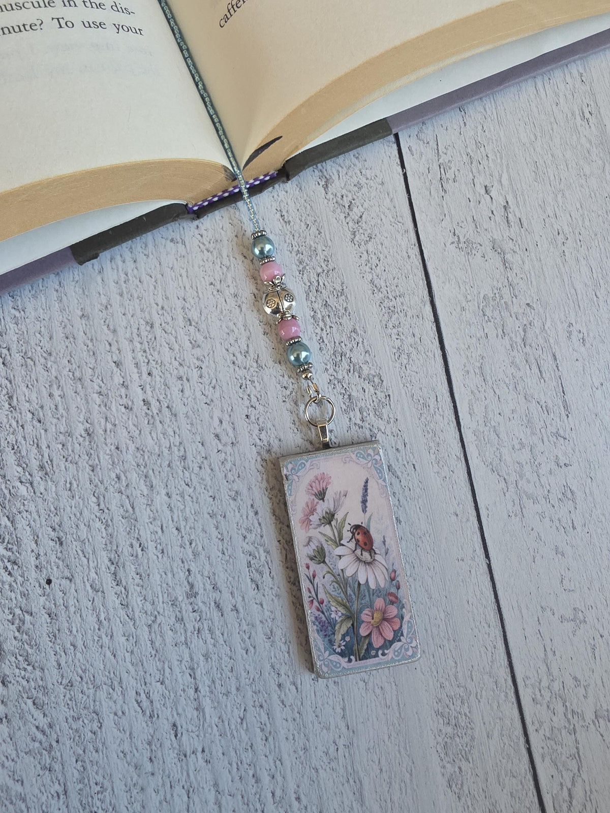 a small, rectangular charm with a floral design, attached to a beaded wire and resting on a wooden surface.