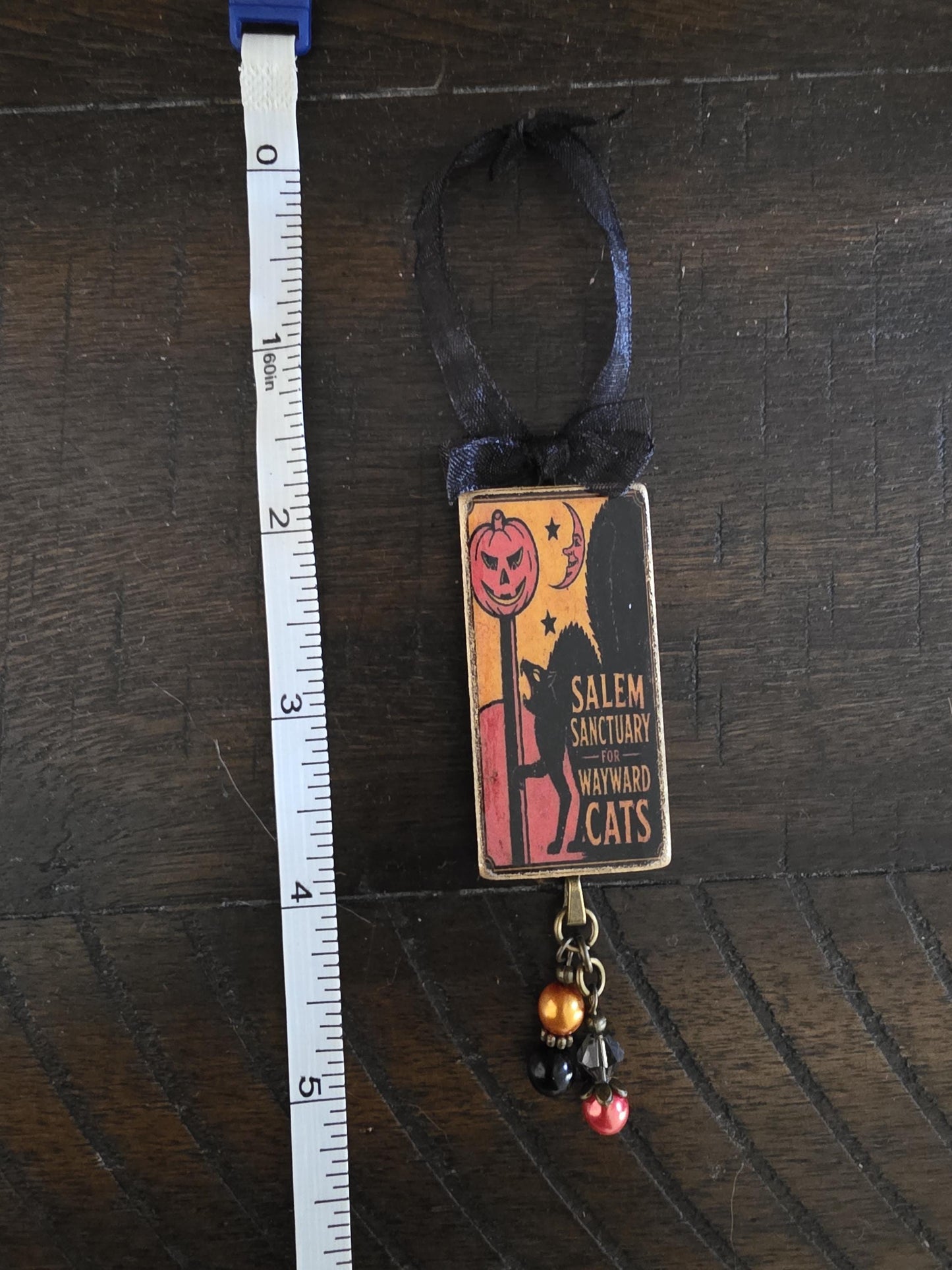 A Halloween-themed ornament with a pumpkin and a cat design, hanging from a ribbon.