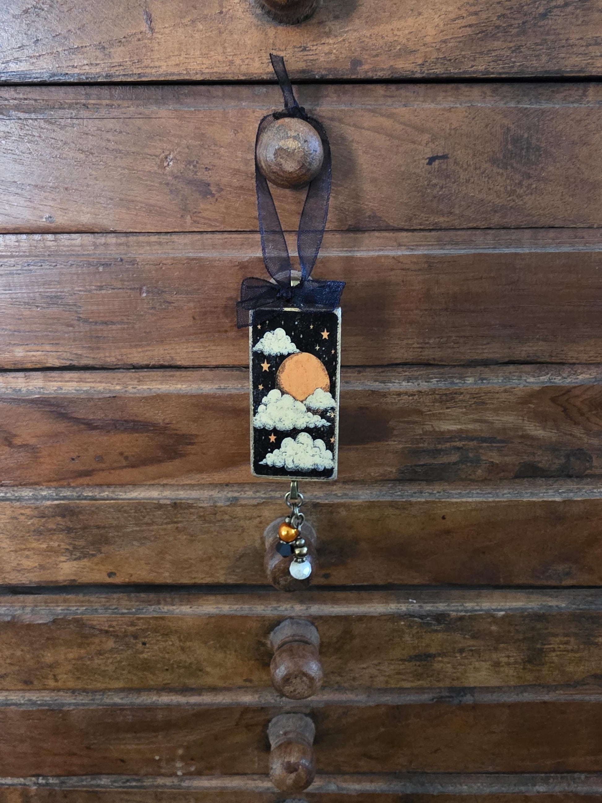 A wooden drawer with a decorative piece hanging from it, featuring a night sky scene with a moon, clouds, and stars.