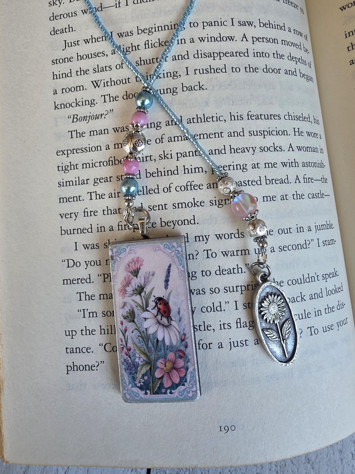 a pendant necklace with a floral design and a small charm in the shape of a flower, resting on an open book.