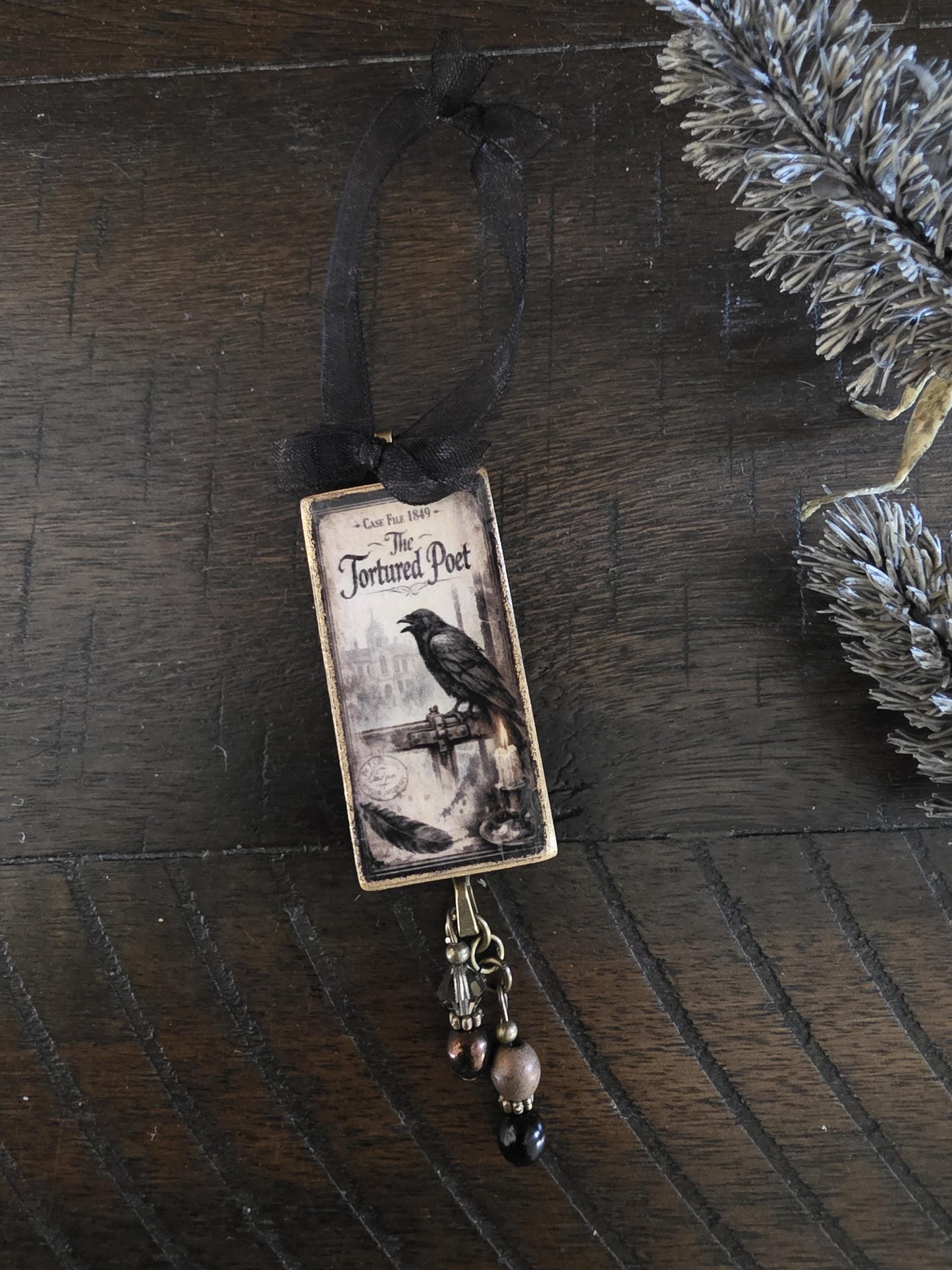 a small decorative ornament with a black ribbon and a black and white illustration of a bird perched on a bridge.
