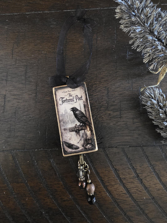 a small decorative ornament with a black ribbon and a black and white illustration of a bird perched on a bridge.
