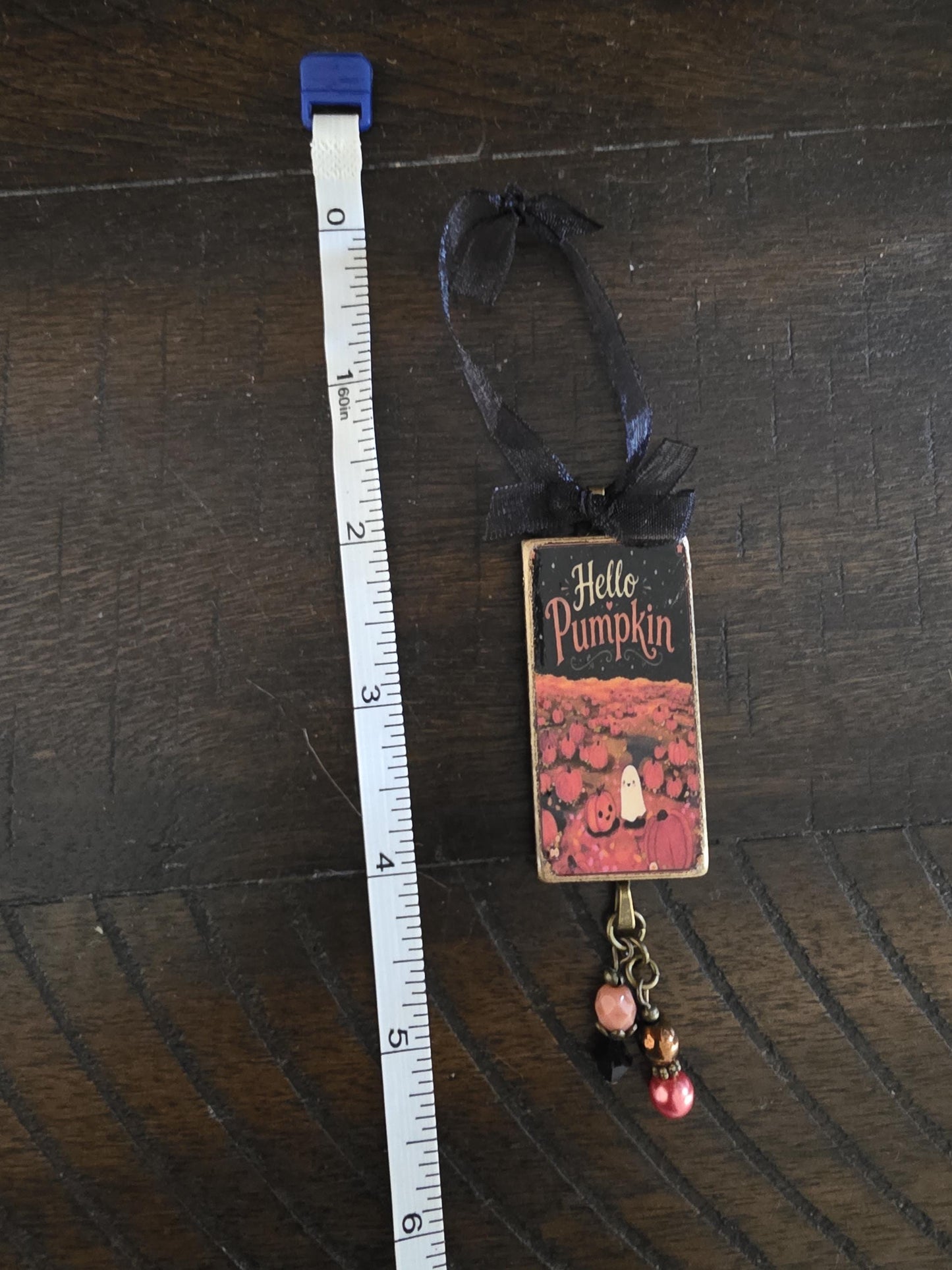 A small decorative item with a black ribbon and a pumpkin-themed design, placed next to a ruler on a wooden surface.