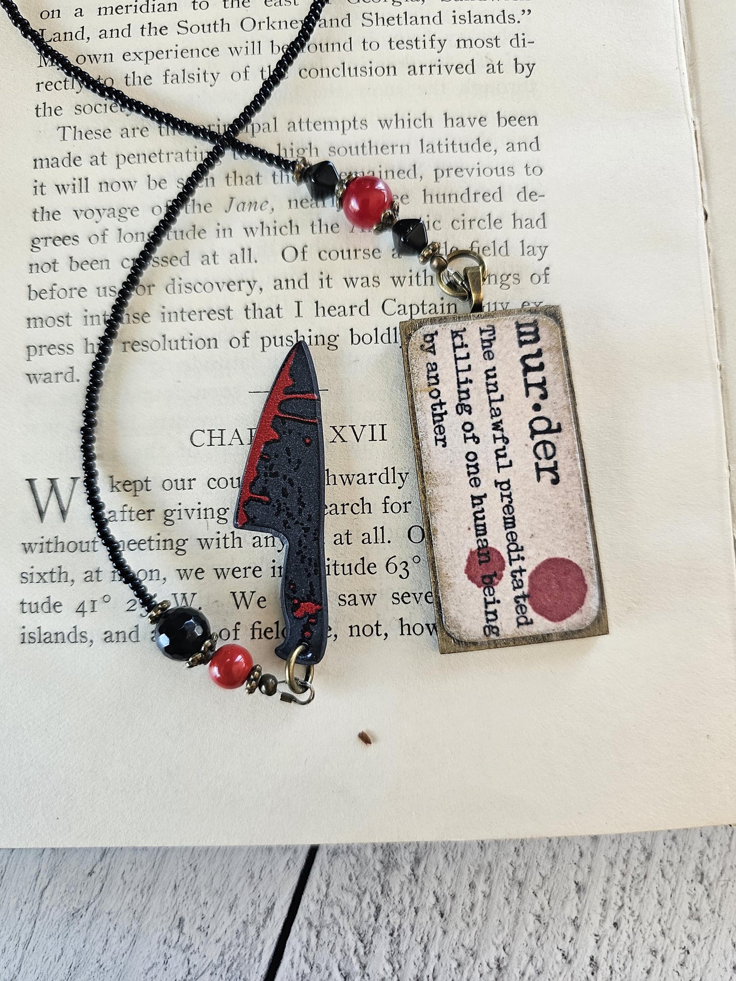 a necklace with a pendant and a book with text on it, placed on a wooden surface.