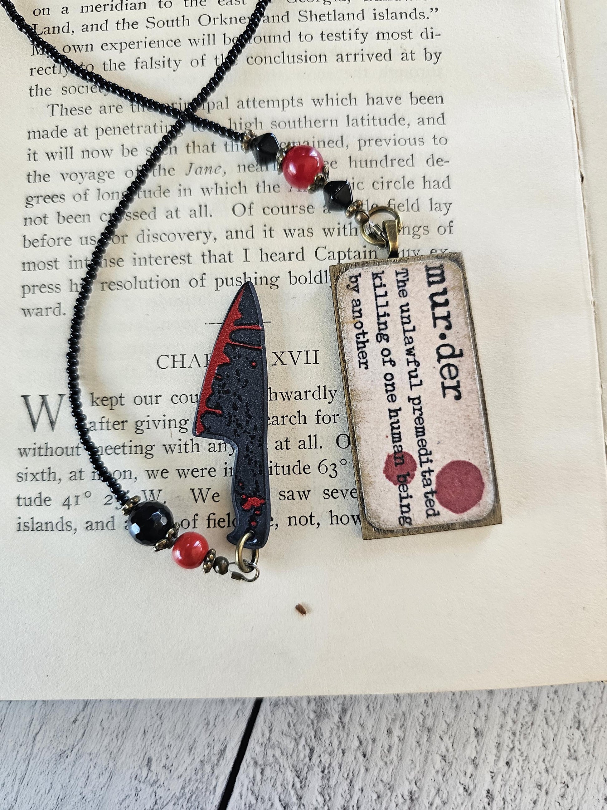a necklace with a pendant and a book with text on it, placed on a wooden surface.