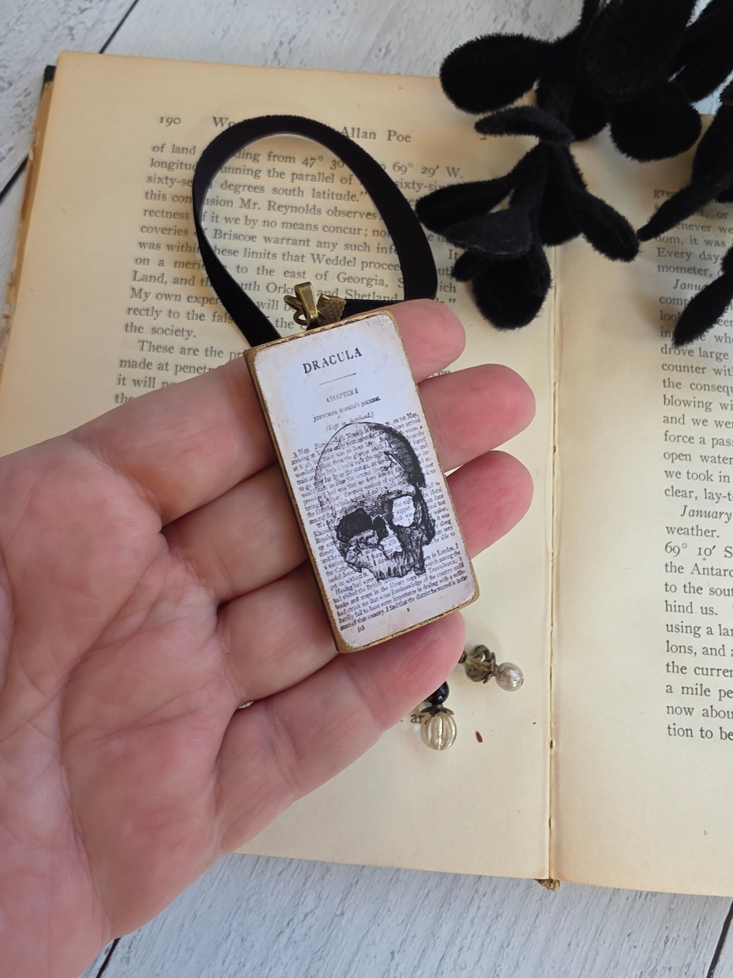 A hand holding a small rectangular object with a skull image on it, placed on top of an open book.