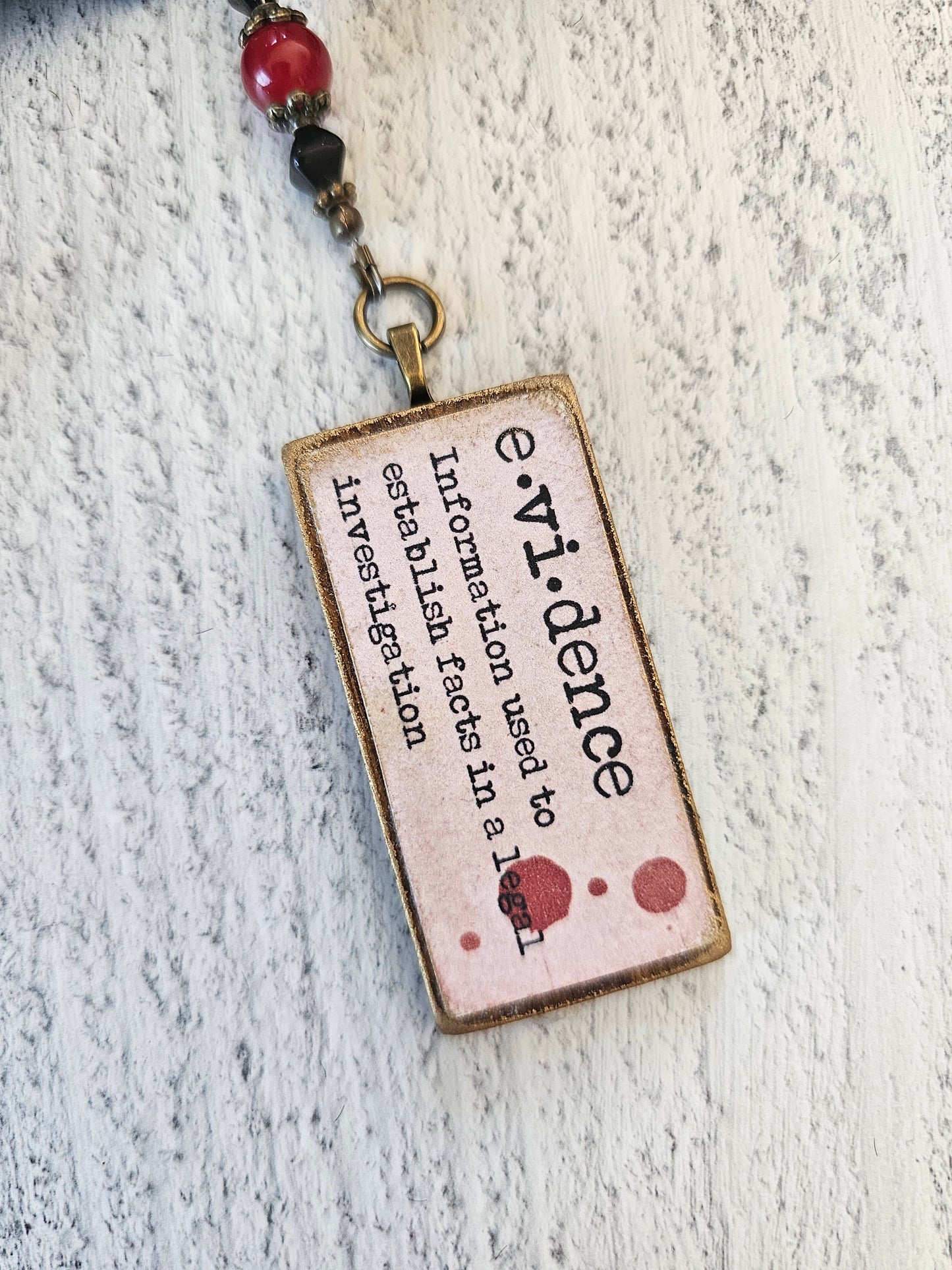 a rectangular metal tag with the word "information" printed on it, attached to a necklace with beads.