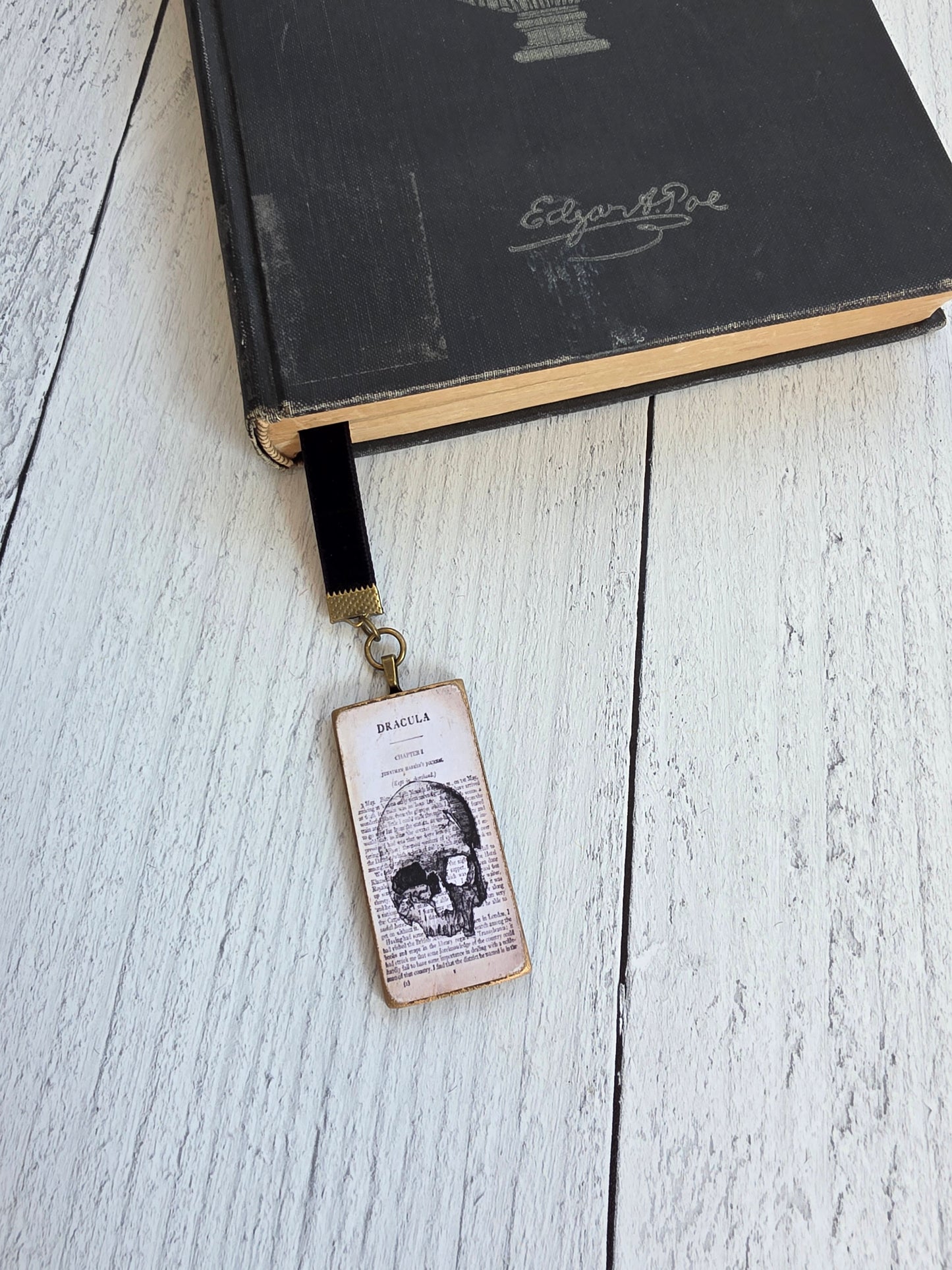A black book with a gold-colored bookmark attached to it, resting on a white wooden surface.
