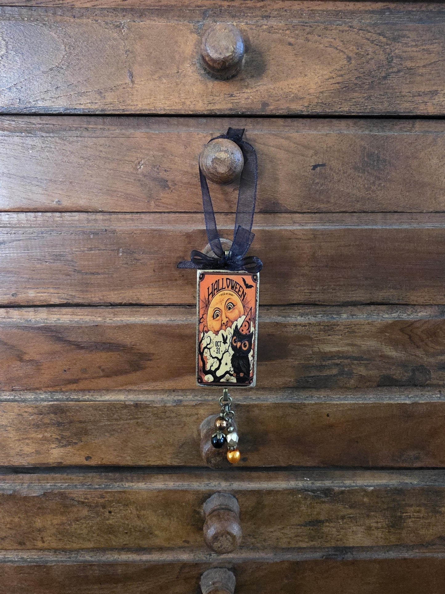 A Halloween-themed decoration is hanging on a wooden dresser, featuring a small, ornate card with a cat illustration and the text "HALLOWEEN".
