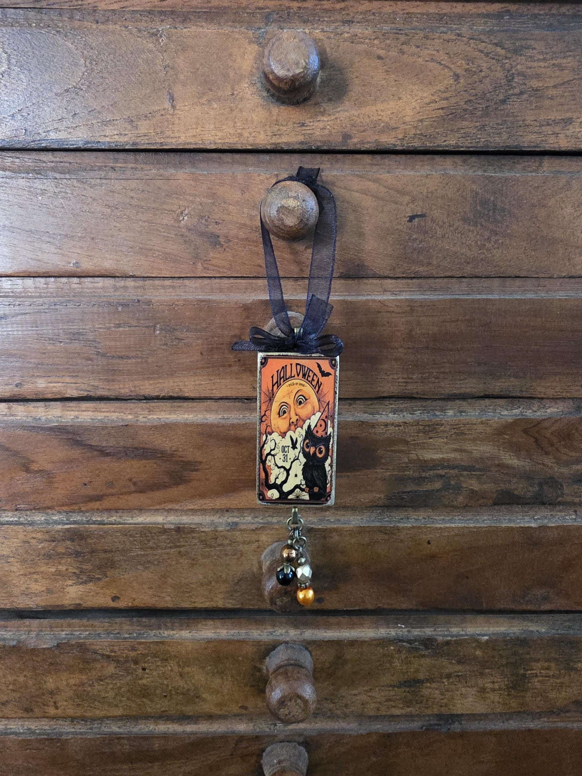 A Halloween-themed decoration is hanging on a wooden dresser, featuring a small, ornate card with a cat illustration and the text "HALLOWEEN".