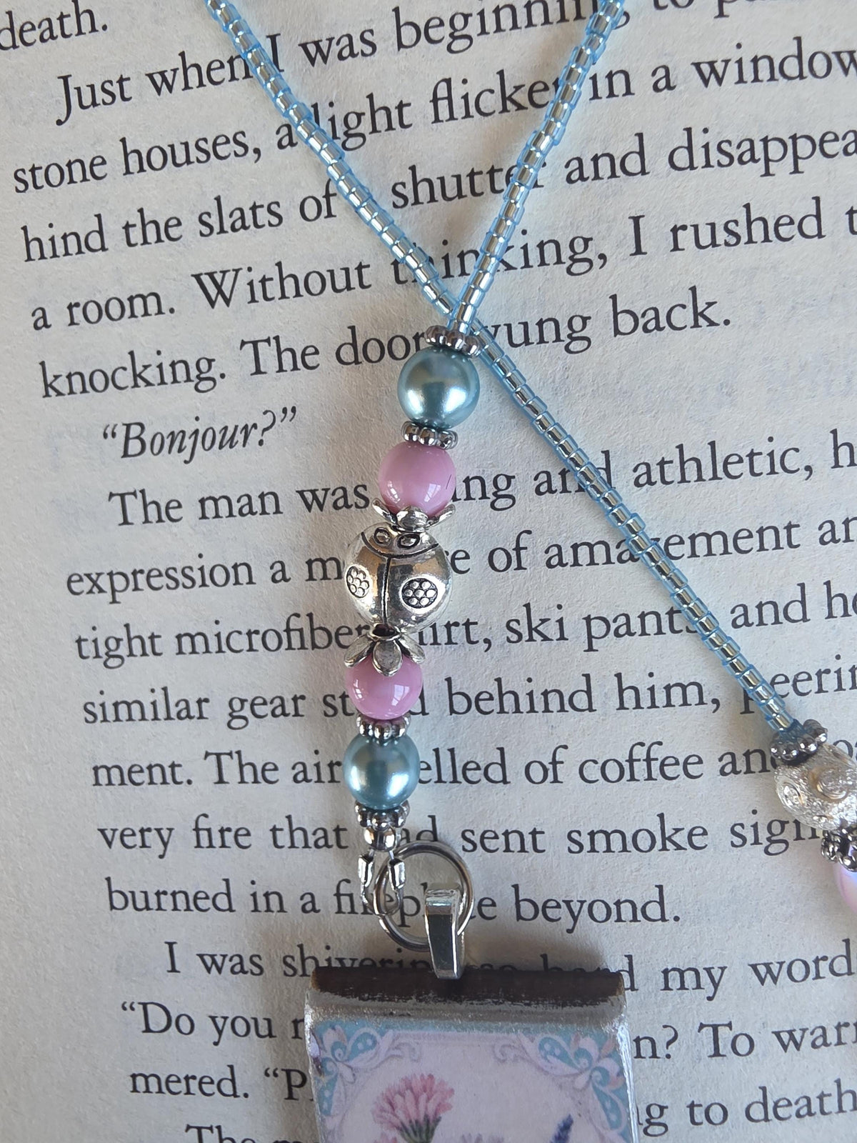 close up of a bookmark pendant, resting on top of a page from a book.