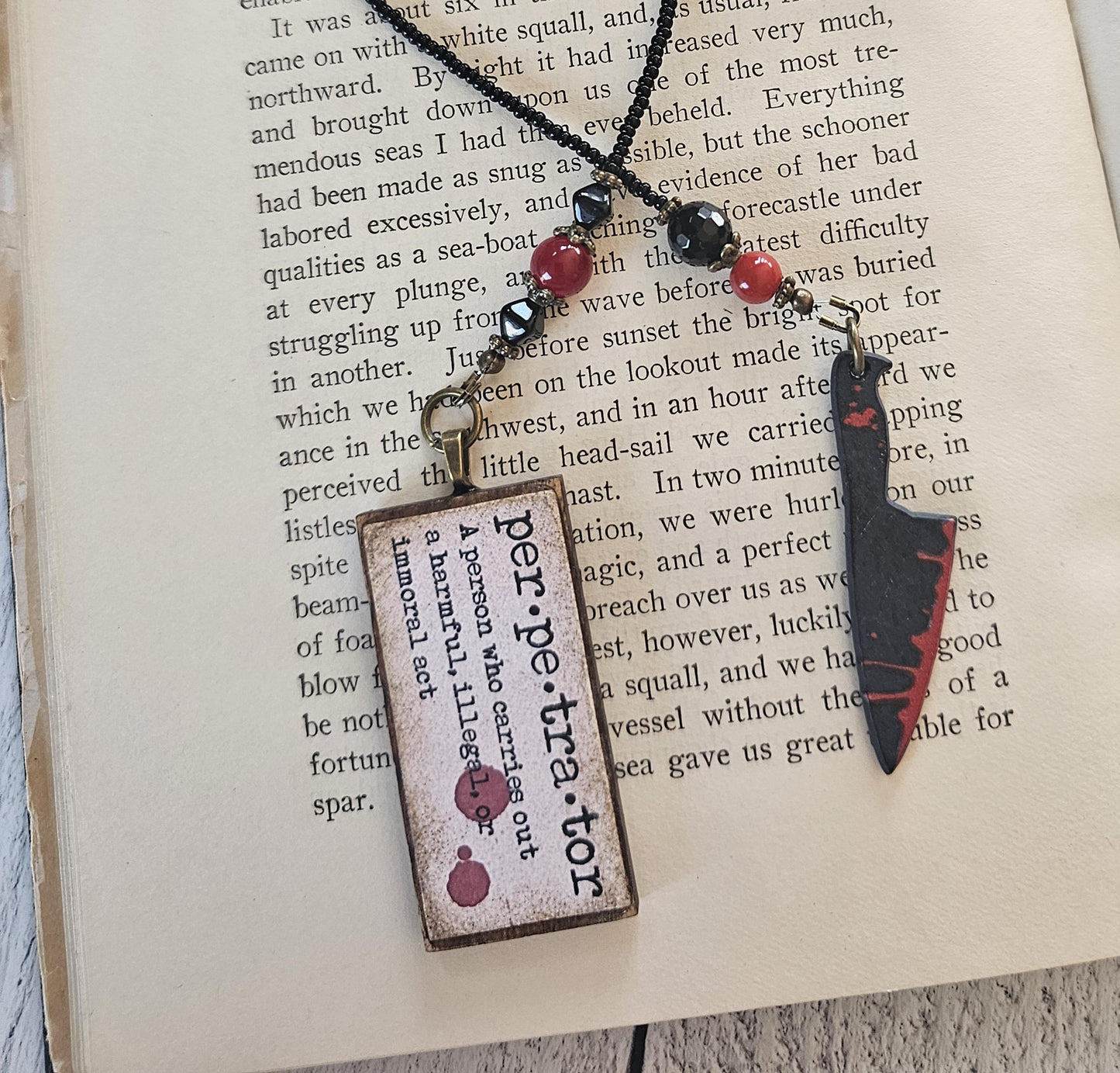 a pendant with a wooden frame and a knife-like design, resting on top of a book.