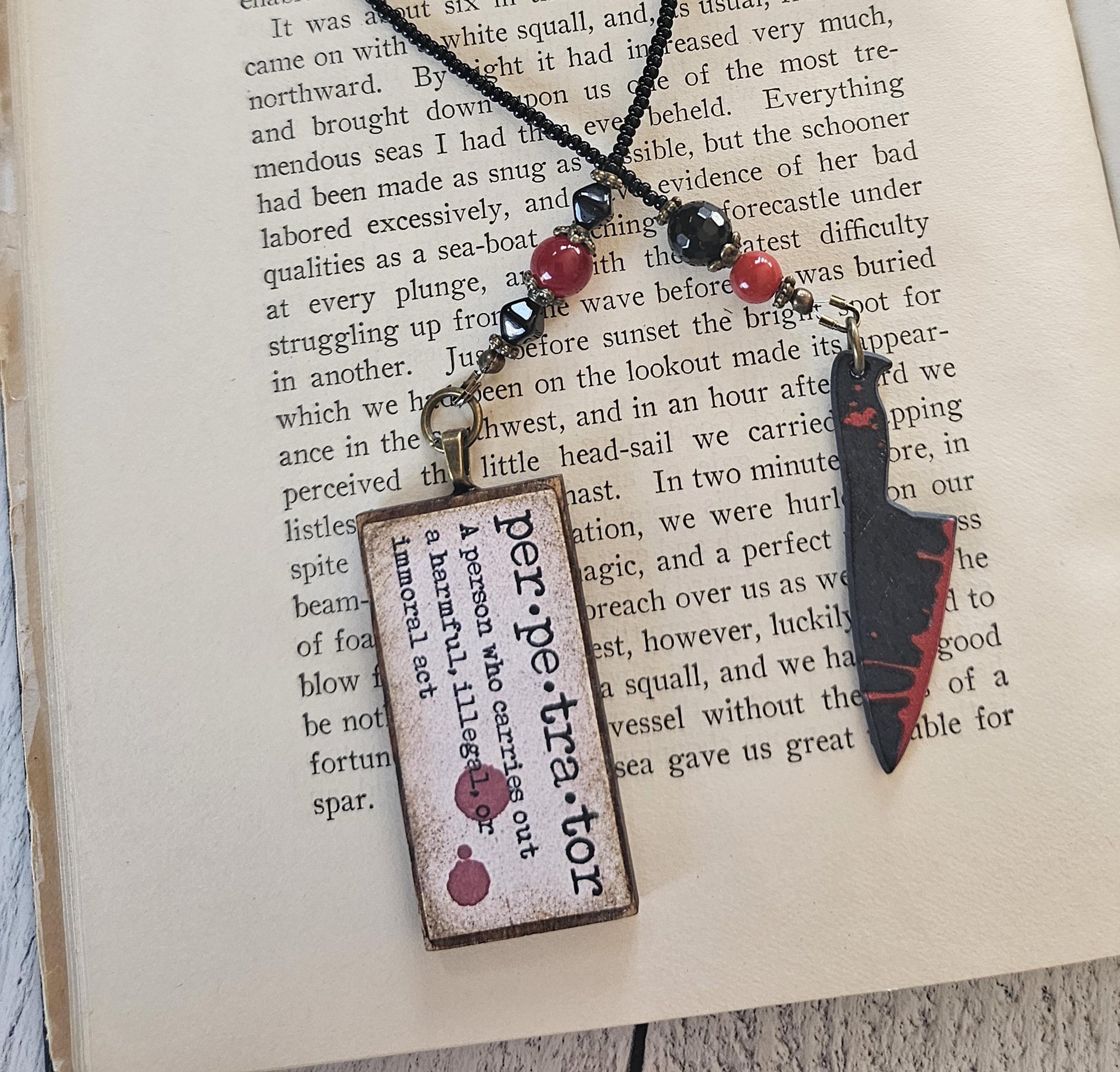 a pendant with a wooden frame and a knife-like design, resting on top of a book.