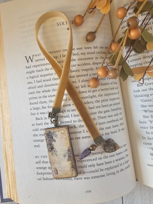 An open book with a beige ribbon bookmark attached to it, along with some dried leaves and berries.