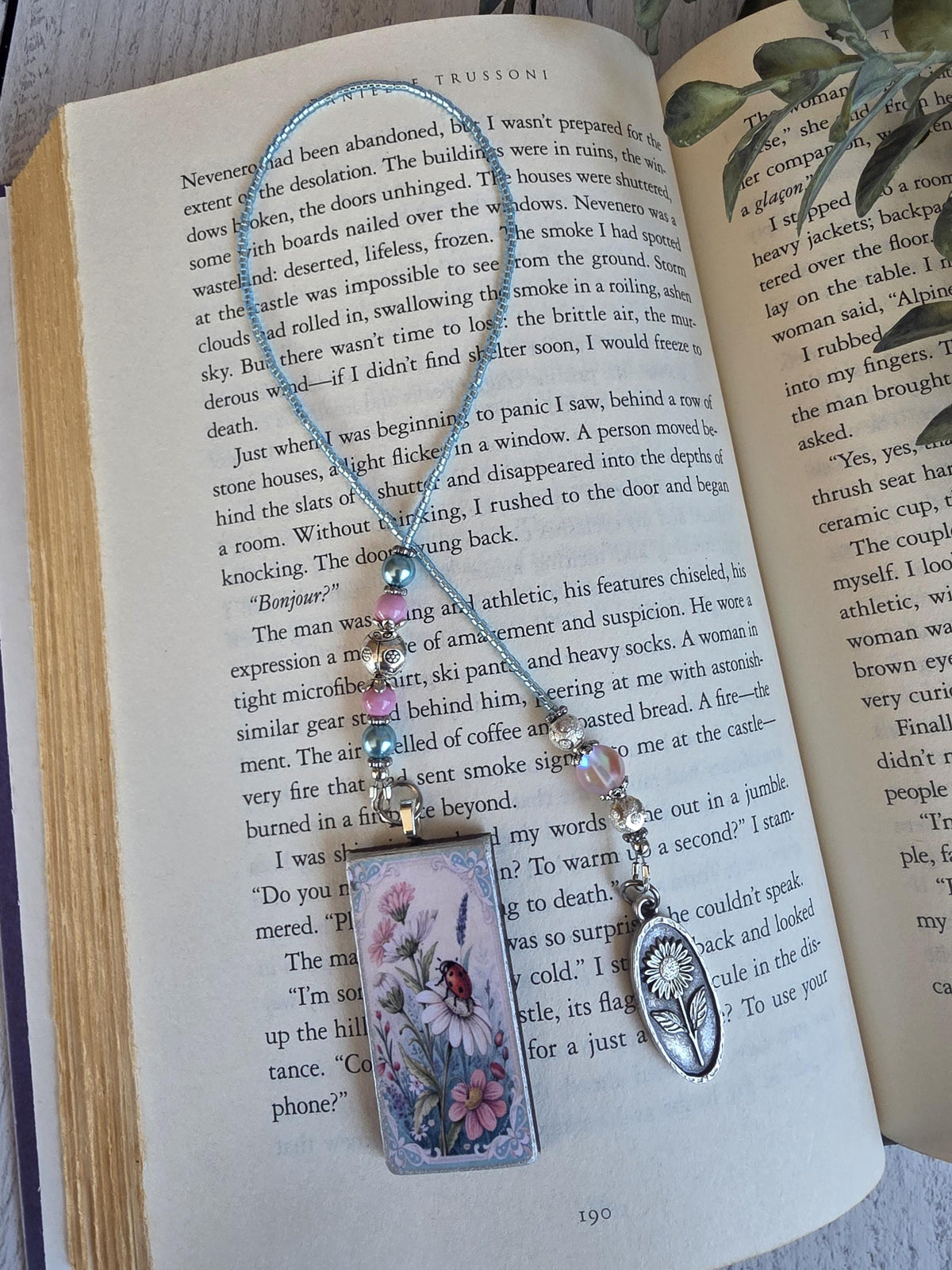 a pendant with a floral design and a charm hanging from a book, with the book open and resting on a surface.