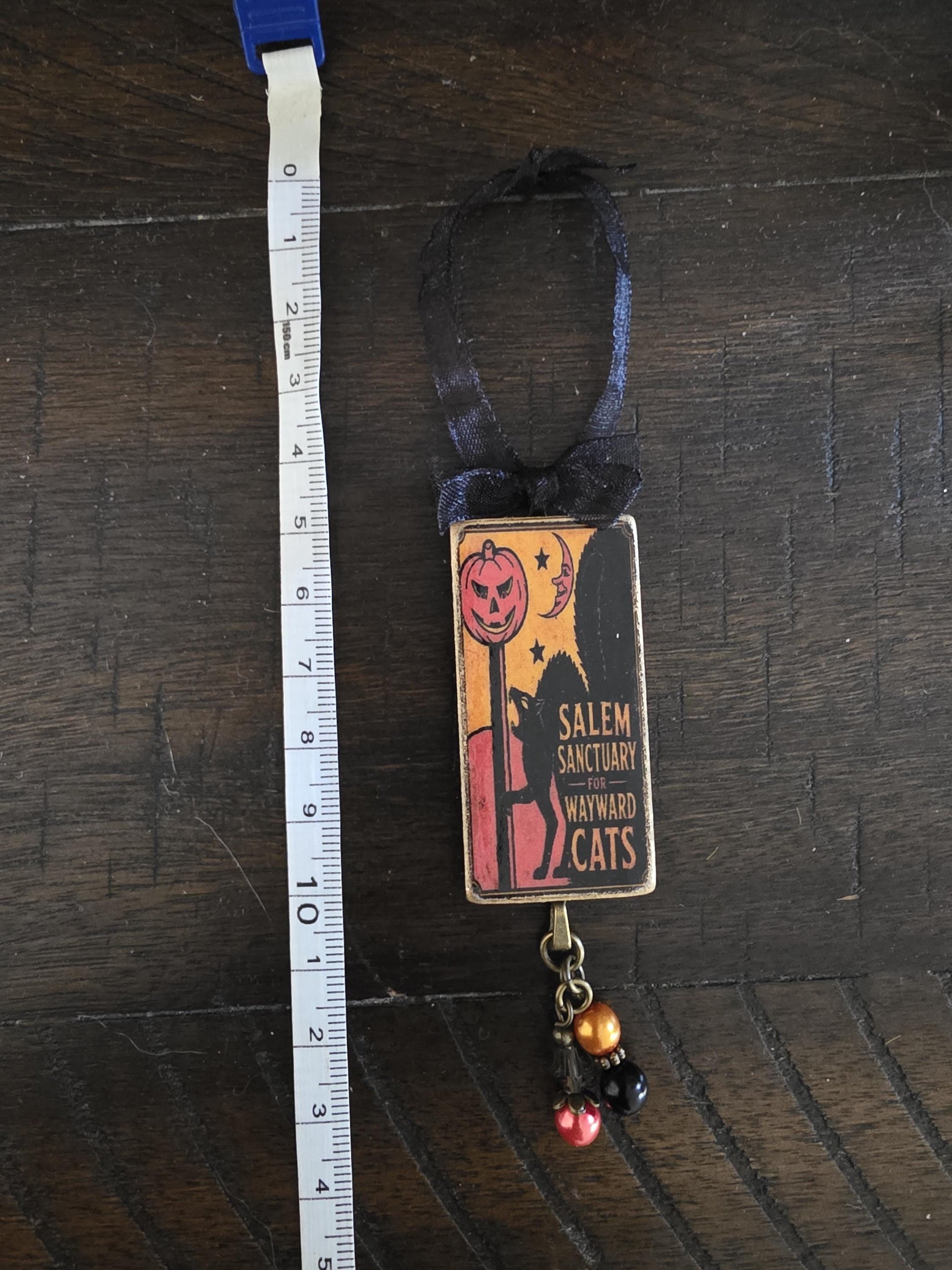 A Halloween-themed ornament with a pumpkin and a cat design, hanging from a ribbon.